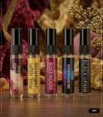 5ml glass perfume tester spray bottles displaying labels for Oud For Greatness, Stronger With You, Oud Rosewood, Oud Montaigne, and Black Opium on a wooden surface against a luxury background.